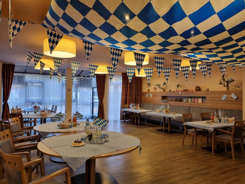 Festlich geschmückter Speisesaal mit blau-weiß karierter Oktoberfest-Dekoration an der Decke und auf den Tischen. Der Raum ist mit Holzmöbeln eingerichtet und vermittelt eine gemütliche, festliche Atmosphäre – bereit für eine Feier im bayerischen Stil.