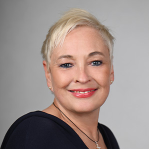 „Porträt einer lächelnden Frau mit Brille und kurzem, hellem Haar – professionelle Aufnahme für die Darstellung des Teams oder der Geschäftsführung.“