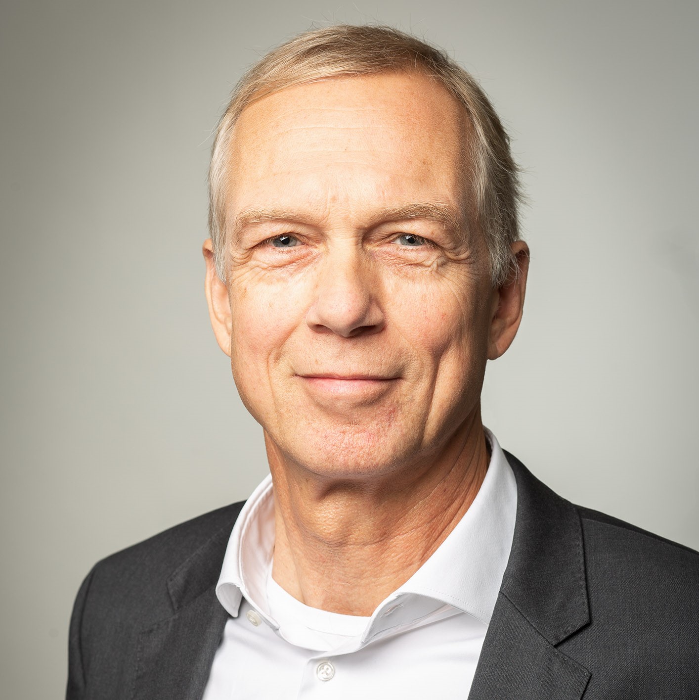 „Porträt eines lächelnden Mannes im Anzug vor neutralem Hintergrund – geeignet für Team- oder Managementvorstellung.“