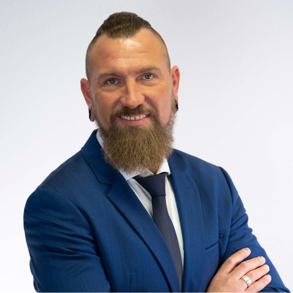 „Porträt eines freundlich blickenden Mannes mit Bart und Anzug vor hellem Hintergrund – ideal zur Darstellung eines Teammitglieds oder Ansprechpartners.“