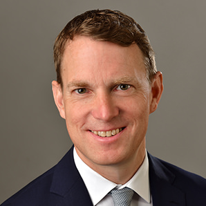 „Porträt eines freundlich lächelnden Mannes im Anzug mit Krawatte vor neutralem Hintergrund – ideal zur Darstellung eines Teammitglieds oder Ansprechpartners.“
