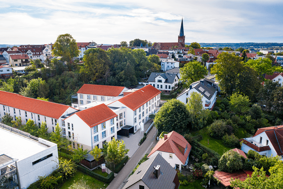 Haupteingang einer modernen Seniorenresidenz mit roter Klinkerfassade, großen Fenstern und einem gepflegten Vorplatz mit Blumenbeet und Sitzbank.